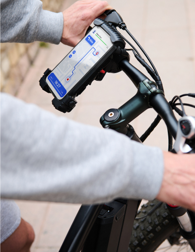 A person is riding and holding the handlebars of a bicycle, and the map screen is clearly visible on a mounted smartphone.