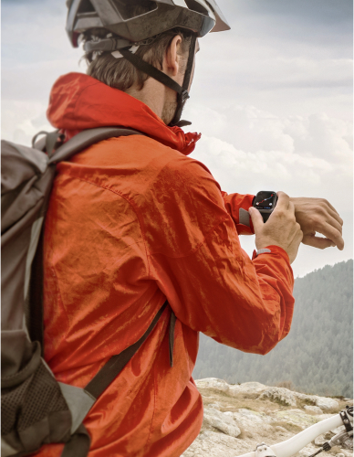 A person wearing a red windbreaker and helmet is operating a smartwatch on a high mountain.